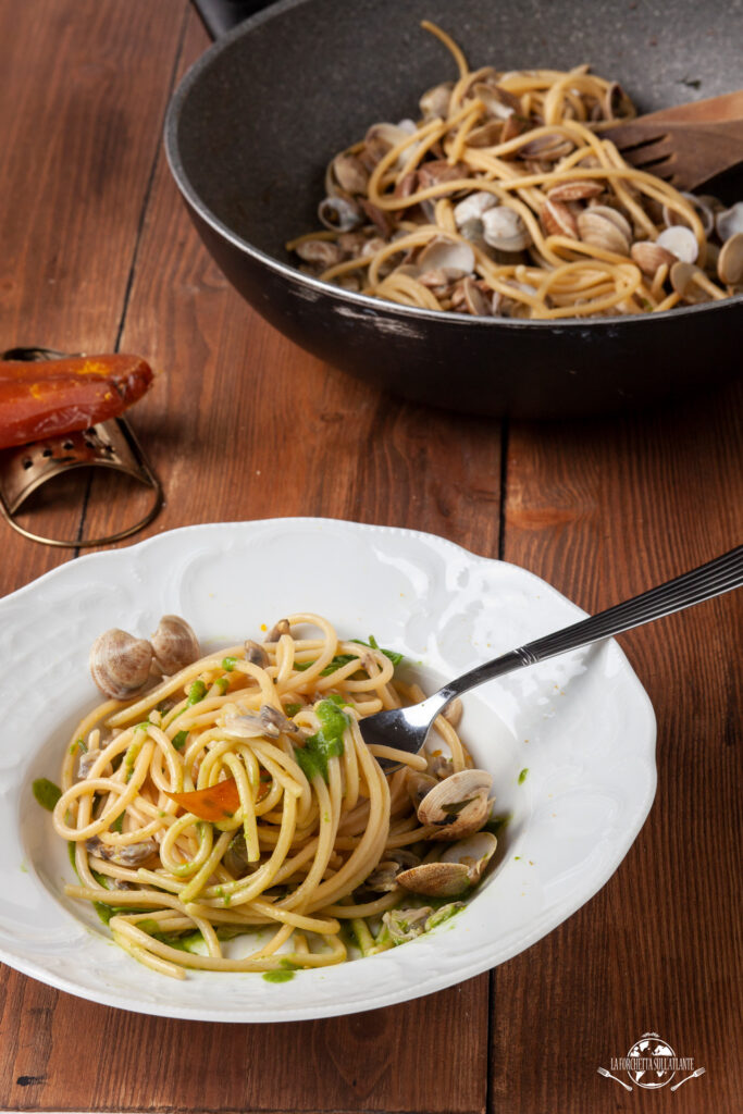 Piatto di spaghettoni con vongole e salsa di salicornia guarnito con scaglie di bottarga e un filo d'olio extravergine.