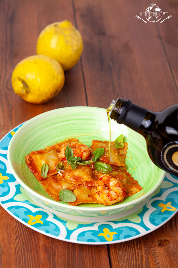 Ravioli fatti in casa al profumo di limone, conditi con bisque di gamberi e un filo di olio Carave, serviti su un piatto decorato con basilico.