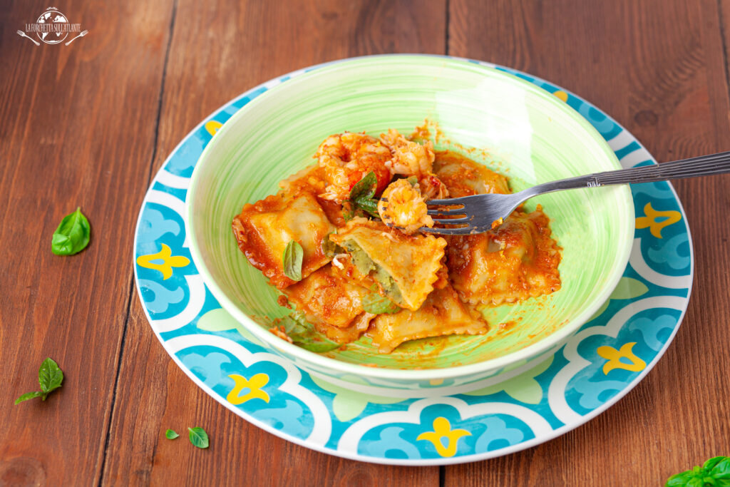 Ravioli fatti in casa al profumo di limone, conditi con bisque di gamberi e un filo di olio Carave, serviti su un piatto decorato con basilico.