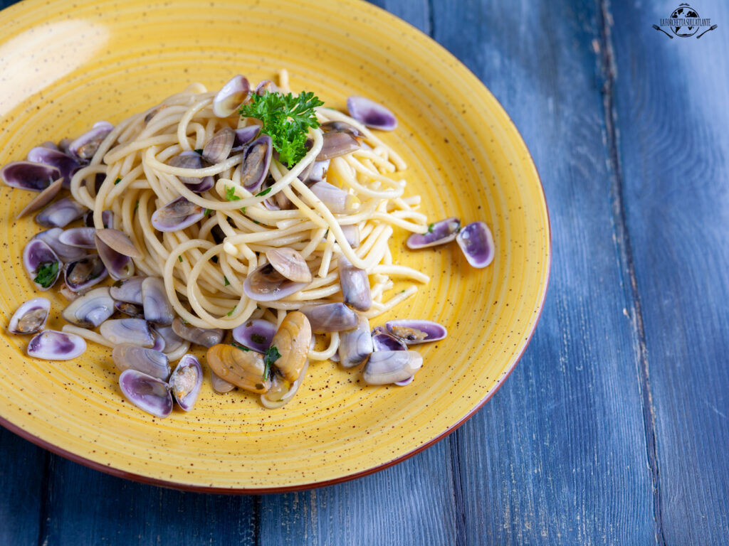 Piatto di Spaghettoni con telline e prezzemolo su sfondo di legno, un piatto semplice e saporito, perfetto per celebrare la fine dell'estate.

