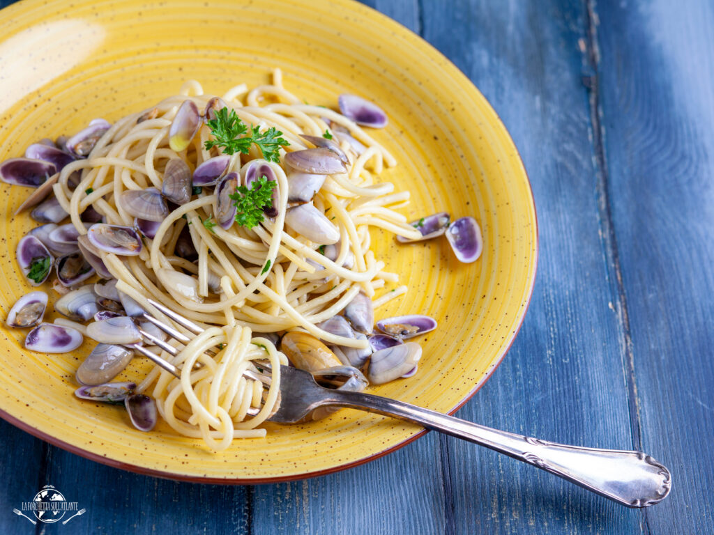 Piatto di Spaghettoni con telline e prezzemolo su sfondo di legno, un piatto semplice e saporito, perfetto per celebrare la fine dell'estate.

