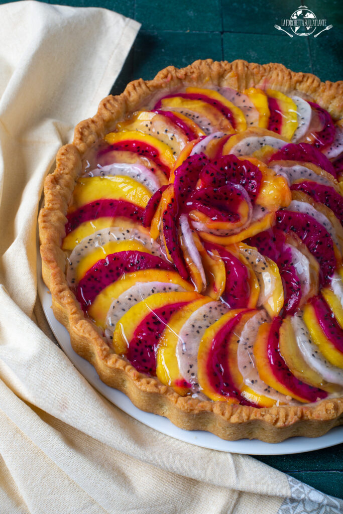 Crostata al mango e dragon fruit con crema pasticcera allo yuzu, decorata con fette di frutta tropicale bianca e magenta, lucidata con gelatina.

