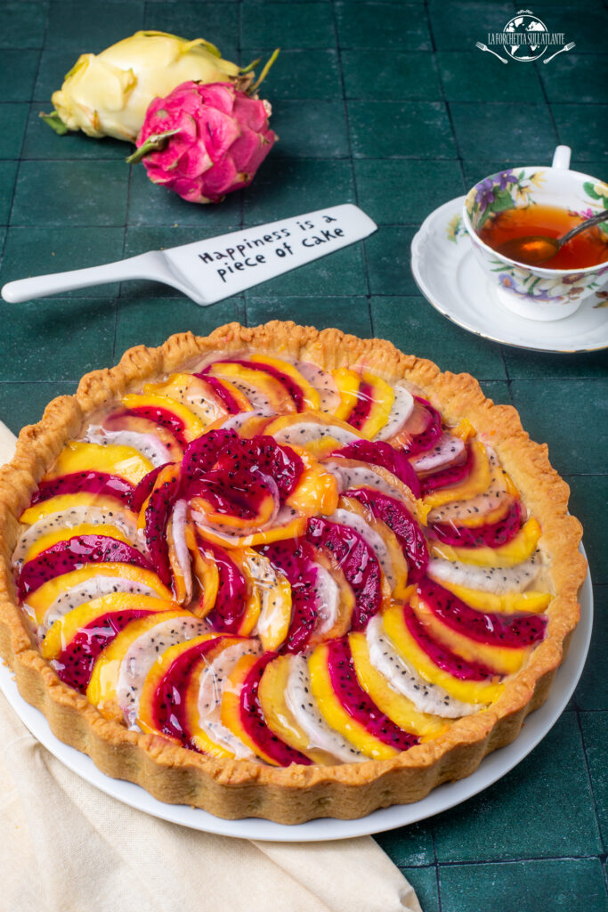 Crostata al mango e dragon fruit con crema pasticcera allo yuzu, decorata con fette di frutta tropicale bianca e magenta, lucidata con gelatina.

